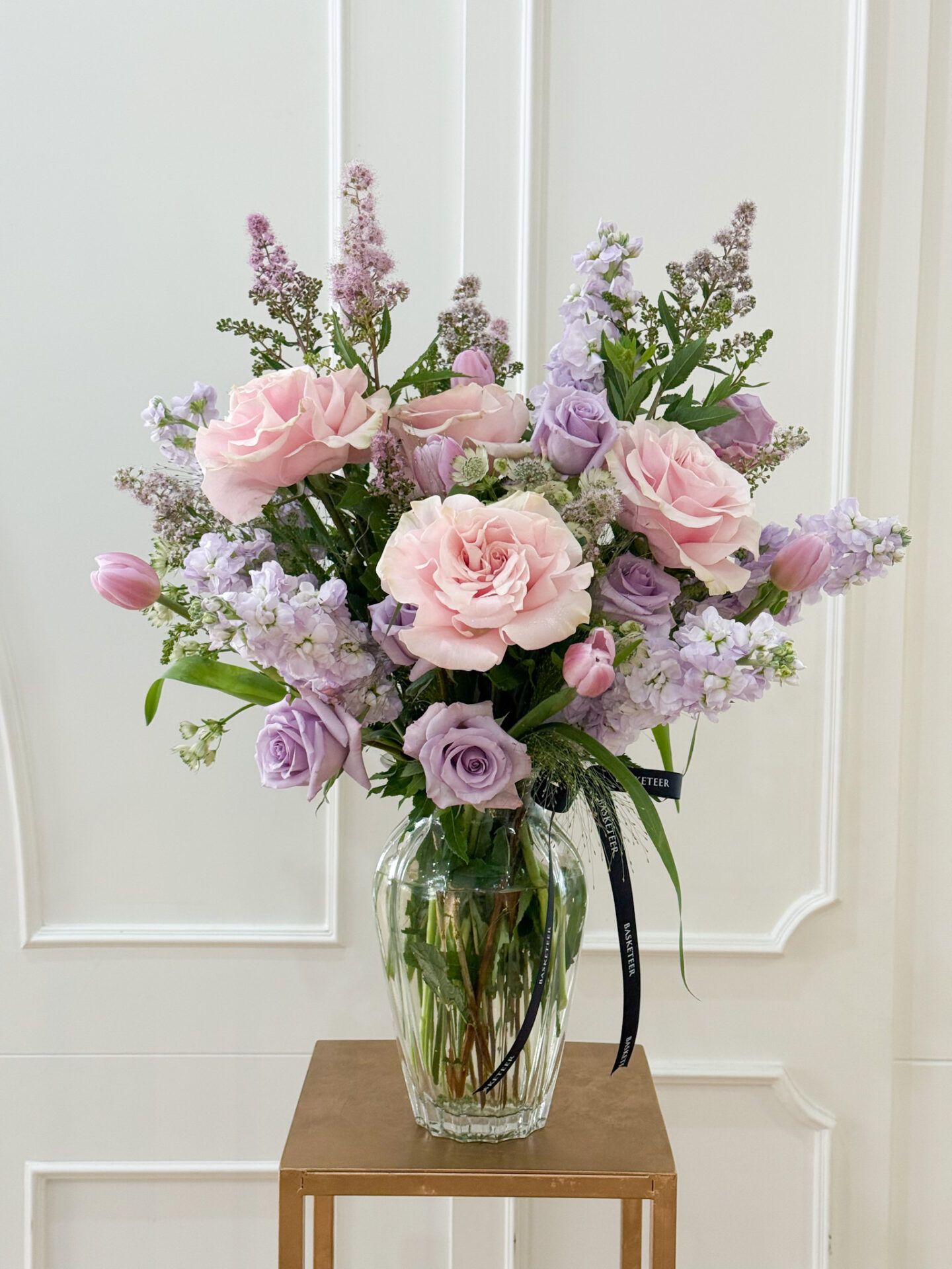 Elegant glass vase with blush roses, lavender roses, tulips, stock, and pastel fillers in pink and purple