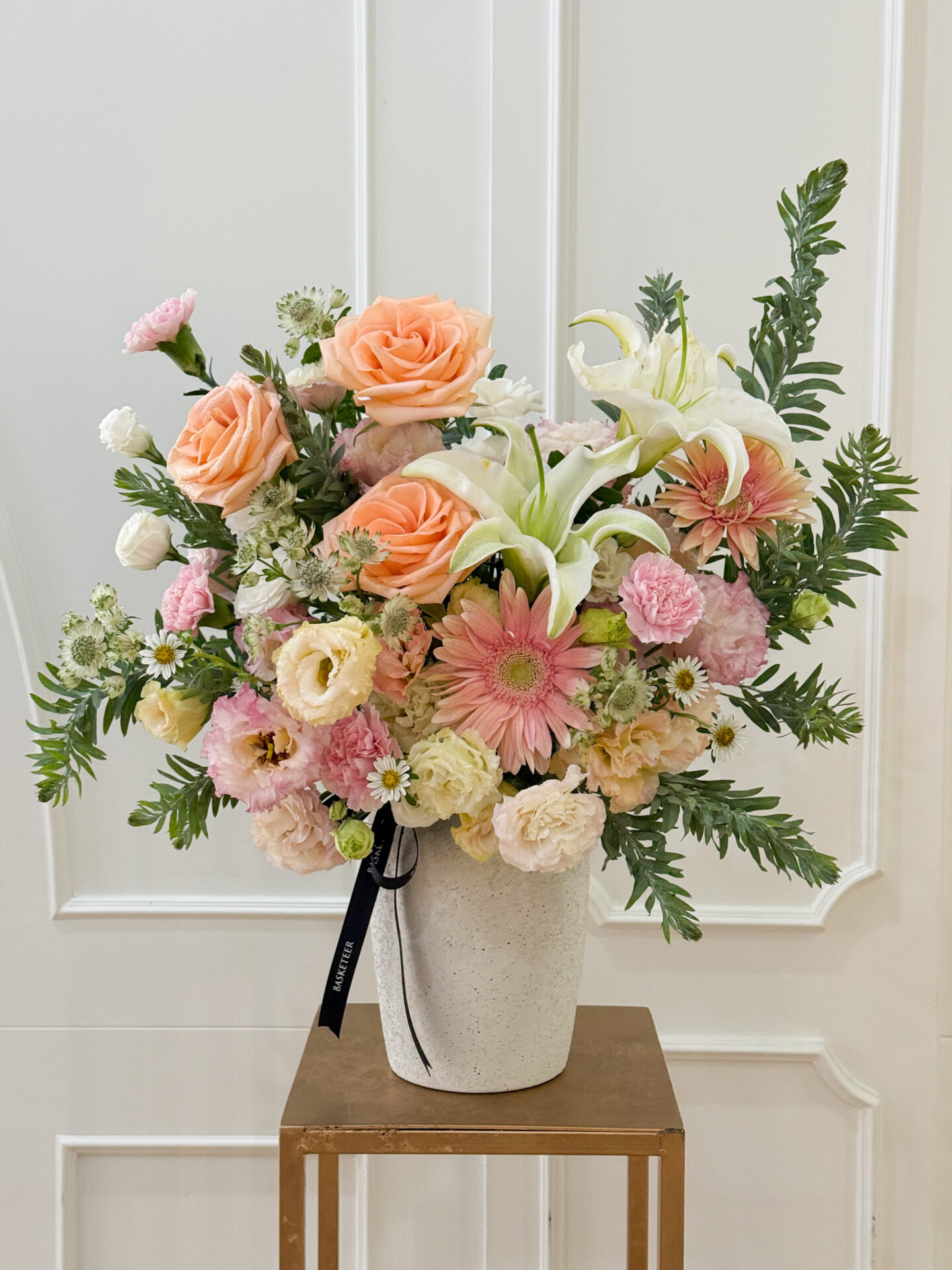 Luxury vase arrangement with peach roses, white lilies, pink gerberas, lisianthus, and pastel carnations.