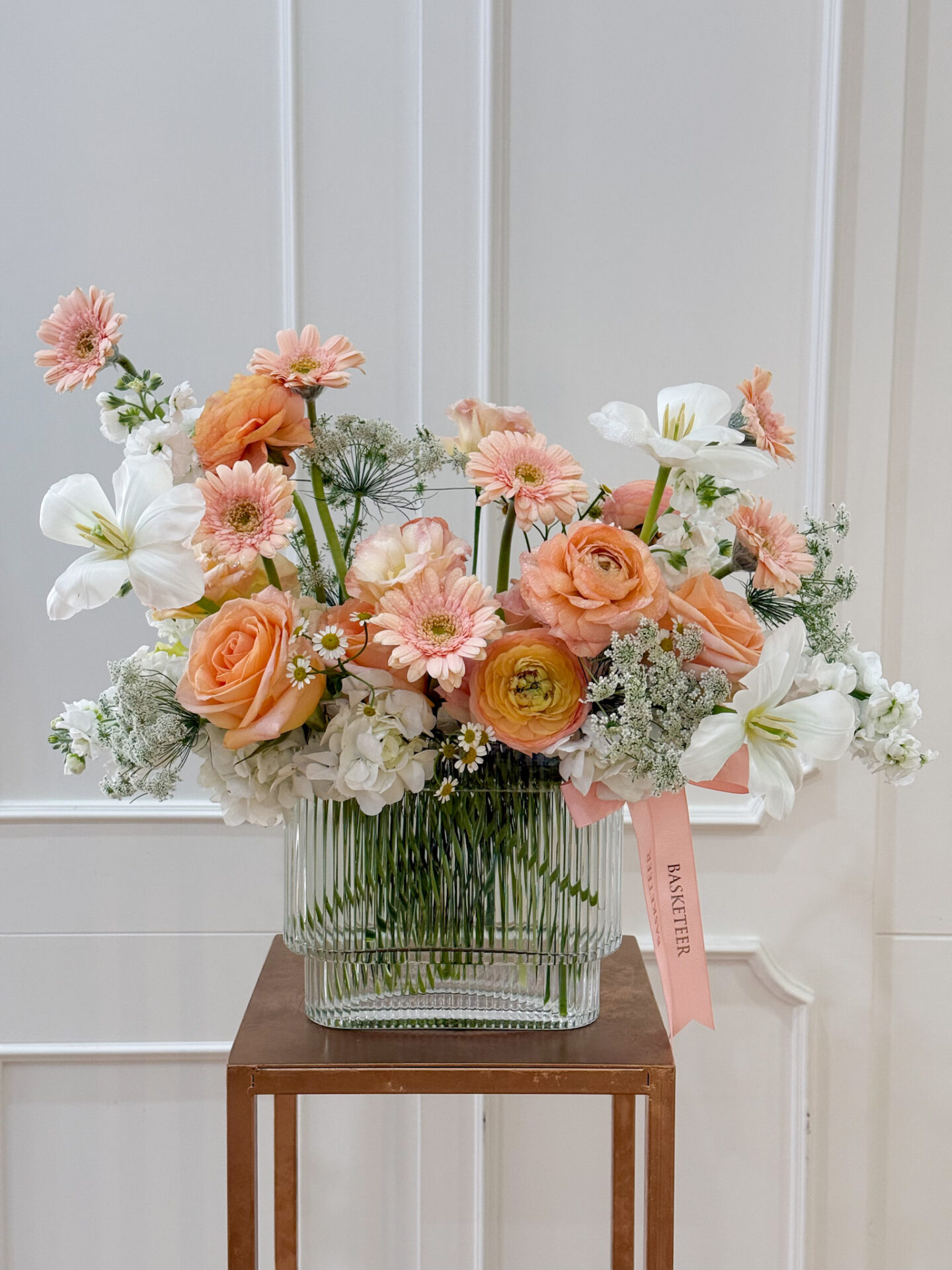 Luxury vase with peach roses, ranunculus, white lilies, peach gerberas, and pastel fillers in a clear glass vase.