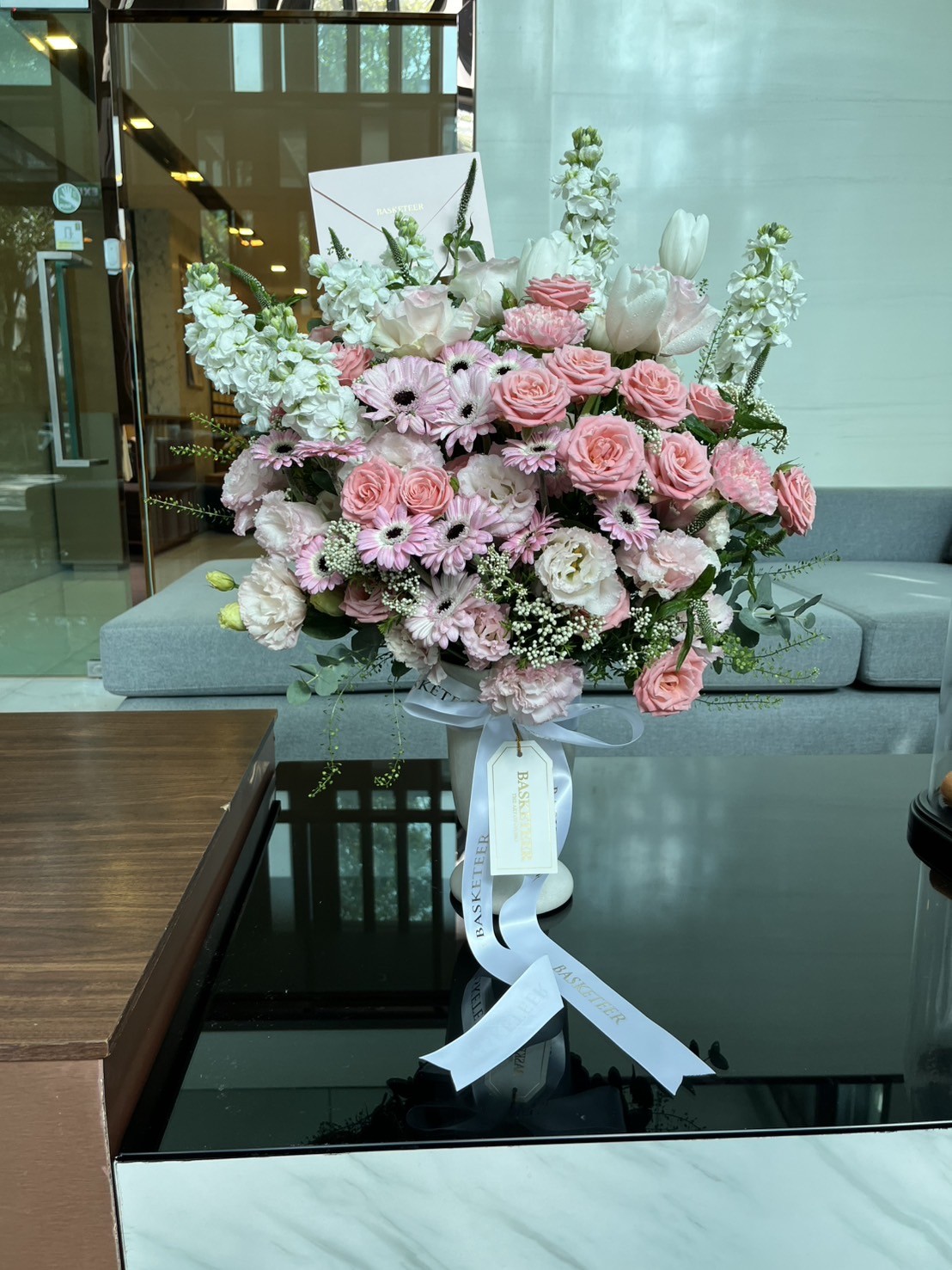 An elegant bouquet of garden roses, pink gerberas, and white stocks in a ribboned vase exudes luxury florals in modern Bangkok style.