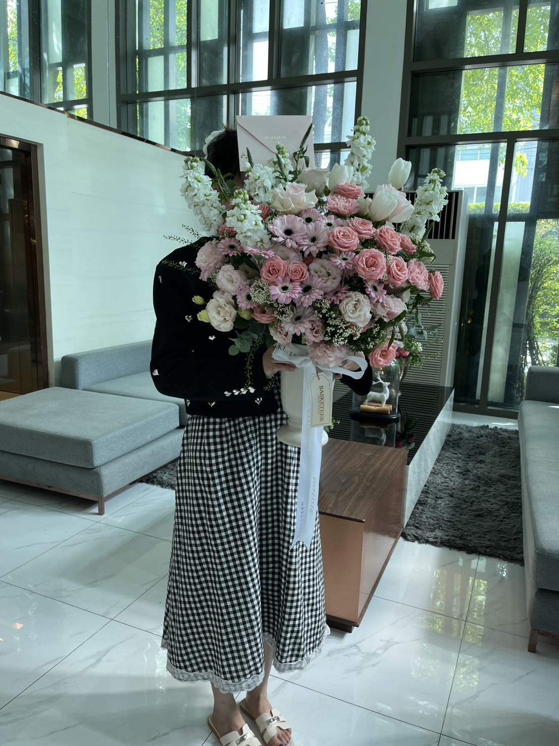 Elegantly dressed, this individual presents a lush Garden Roses and White Stock bouquet with Pink Gerbera in a light-filled Bangkok interior.