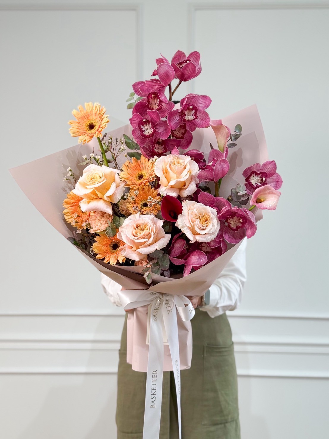 An elegantly wrapped Modern Luxe Bouquet of peach roses, pink orchids, and orange gerberas is presented for luxury delivery in Bangkok.