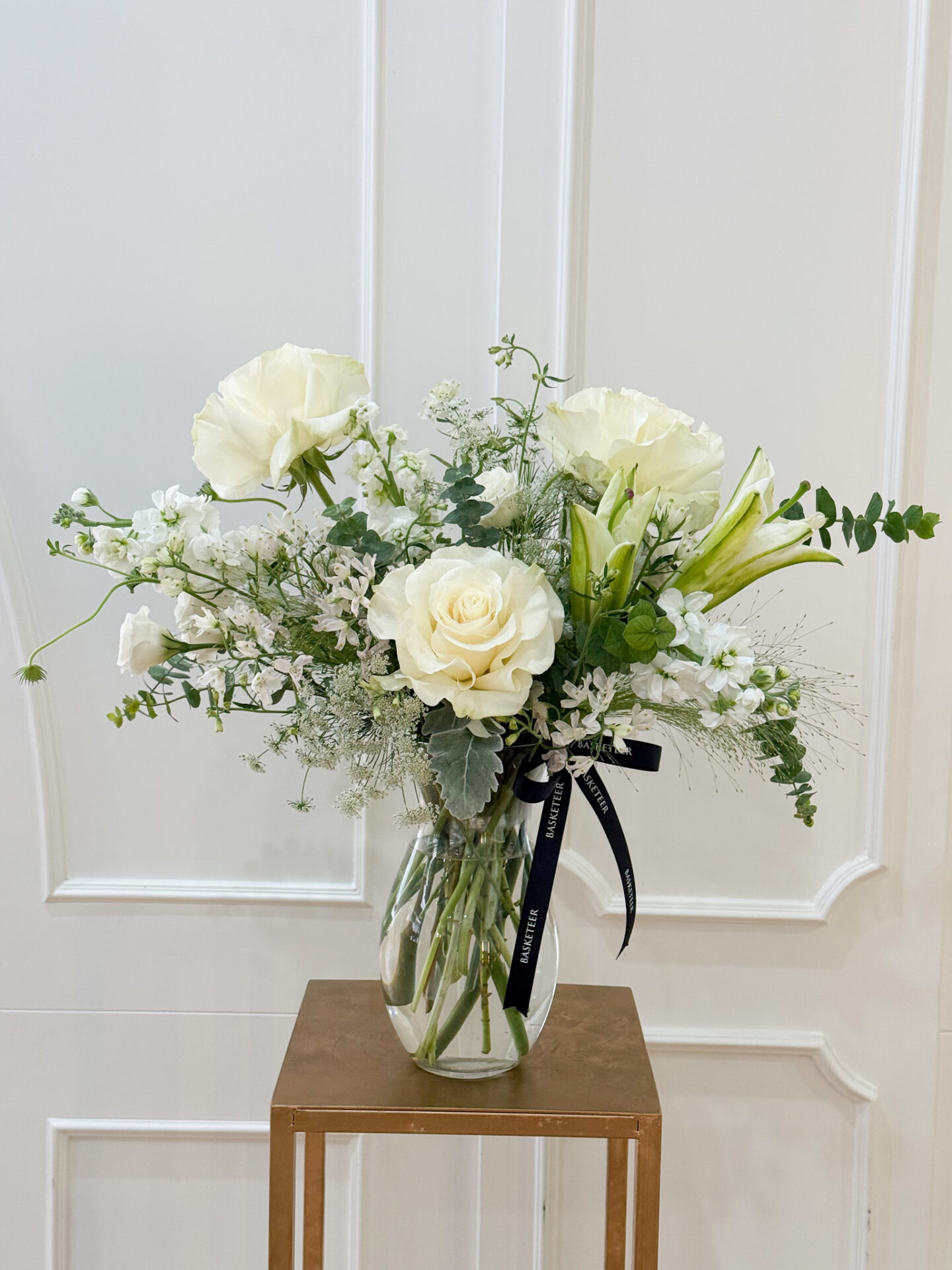 Elegant vase with white roses, white lilies, and fresh greenery in a clear glass vase.
