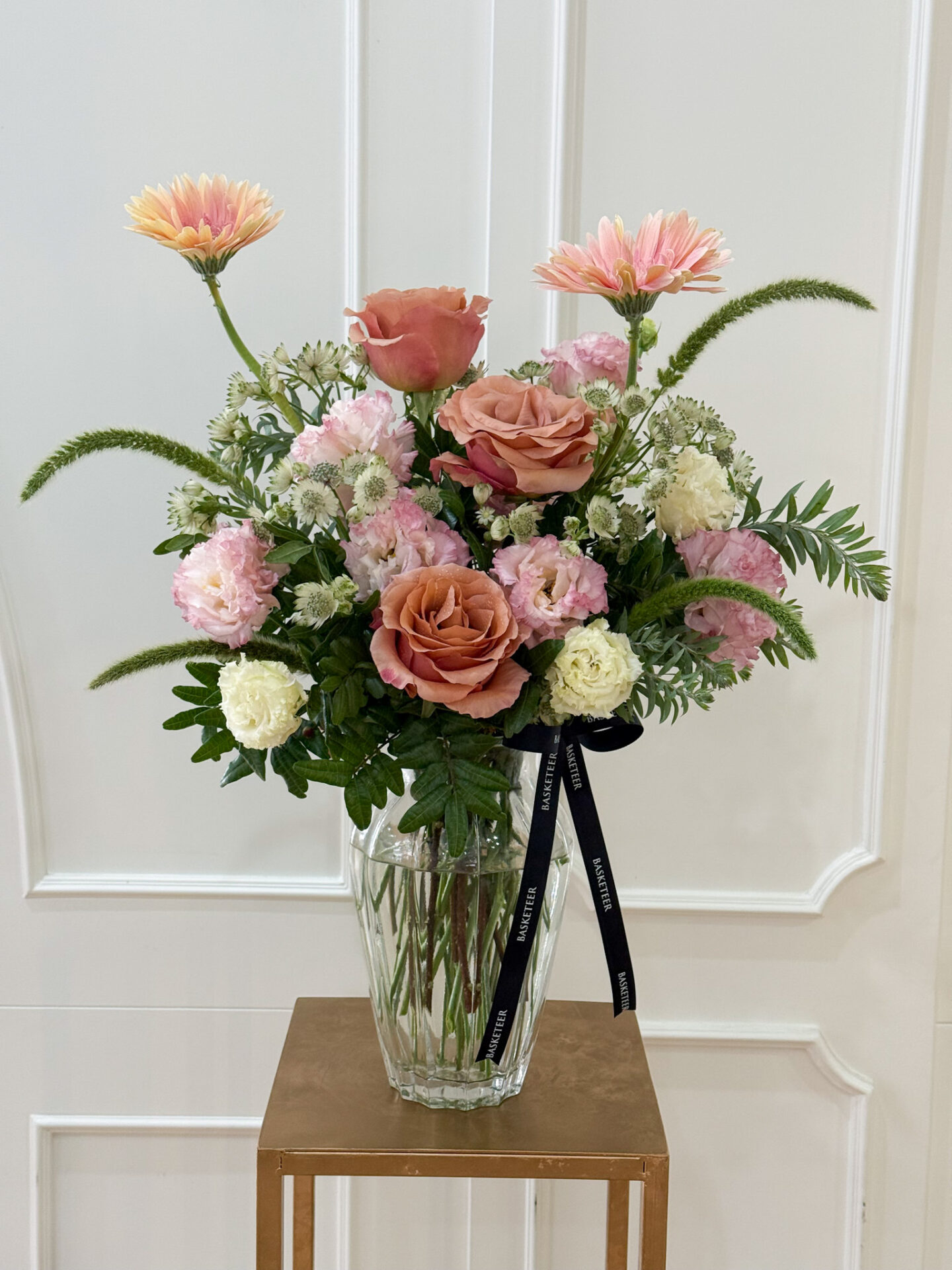 Elegant vase with amber peach roses, peach gerberas, pink lisianthus, white carnations, and greenery.