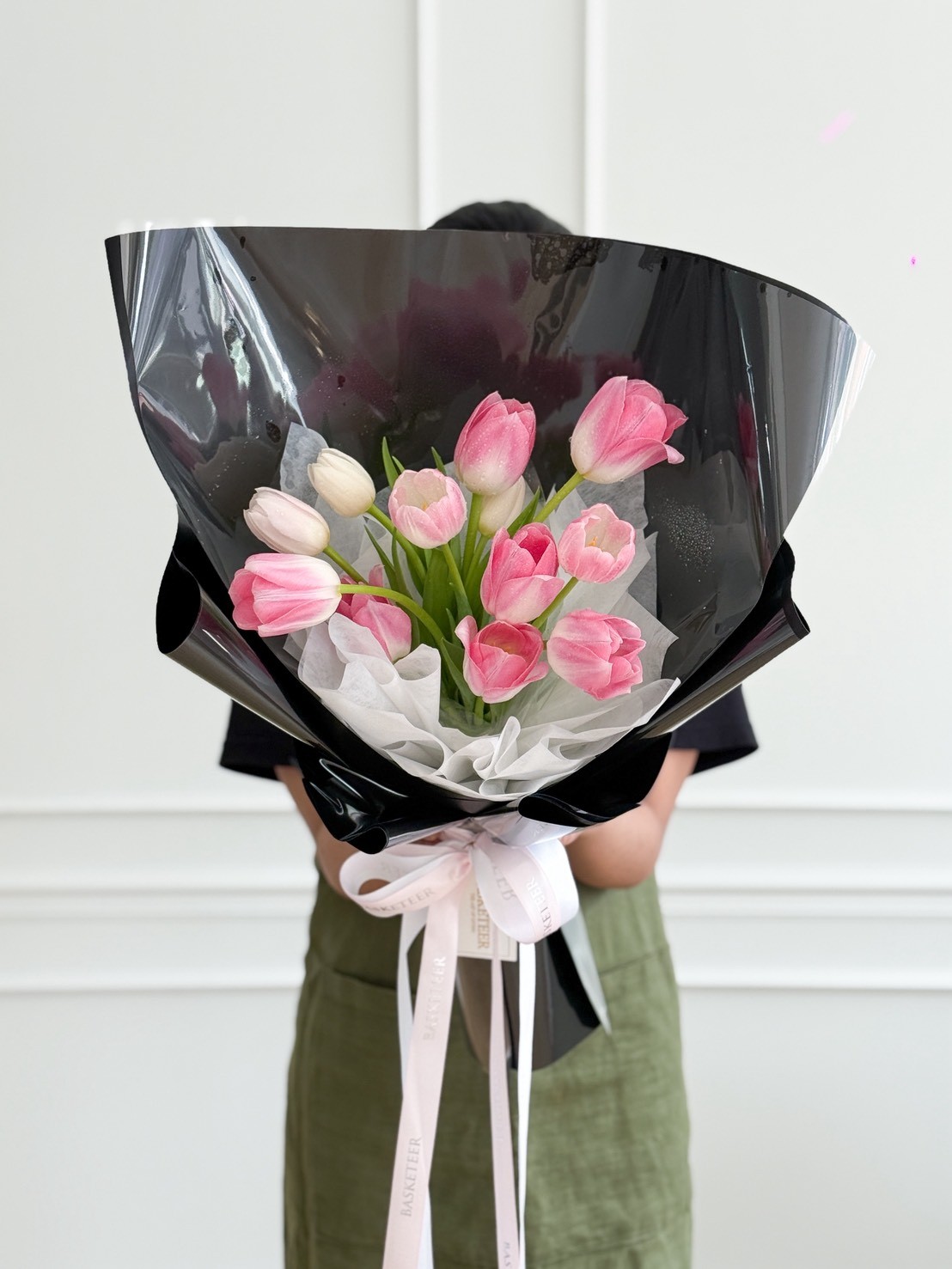 Stylish bouquet of pink tulips with a few white tulips, wrapped in black glossy and white paper with a Basketeer ribbon.
