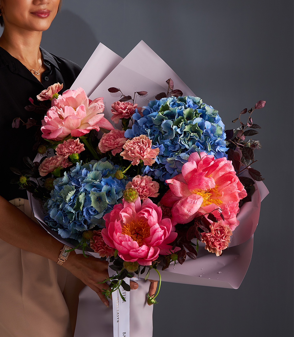 Luxury bouquet with pink peonies, blue hydrangeas, and carnations wrapped in pastel paper.