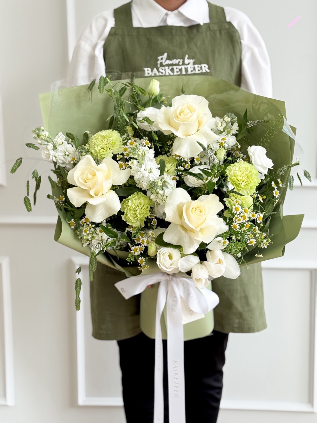 Elegant bouquet with white roses, green carnations, lisianthus, and delicate fillers wrapped in green paper.