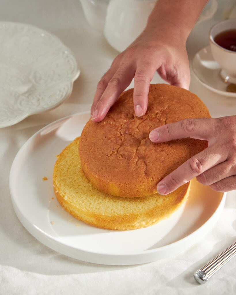 Baker lifting the top layer of sponge cake at Charlotte Bakery Bangkok