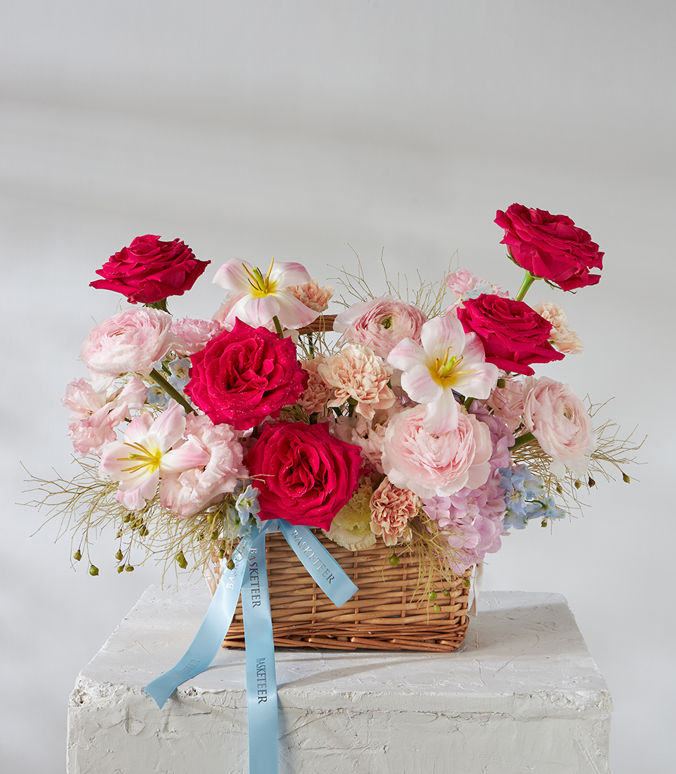 Front view of wicker basket bouquet with red roses, pink ranunculus and white lilies.