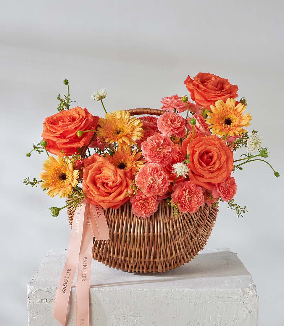Front view of orange rose, carnation and gerbera basket bouquet.