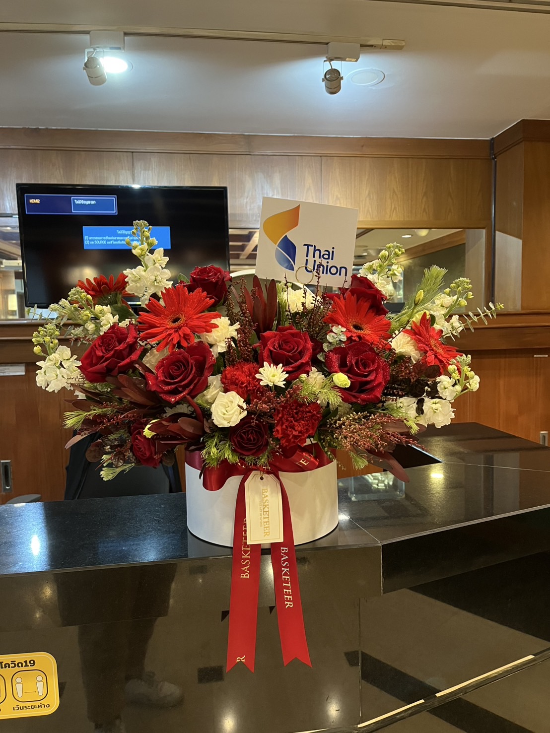 A large arrangement of red and white flowers, including White O’Hara Roses and gerberas, sits in a white hatbox with a red ribbon labelled 