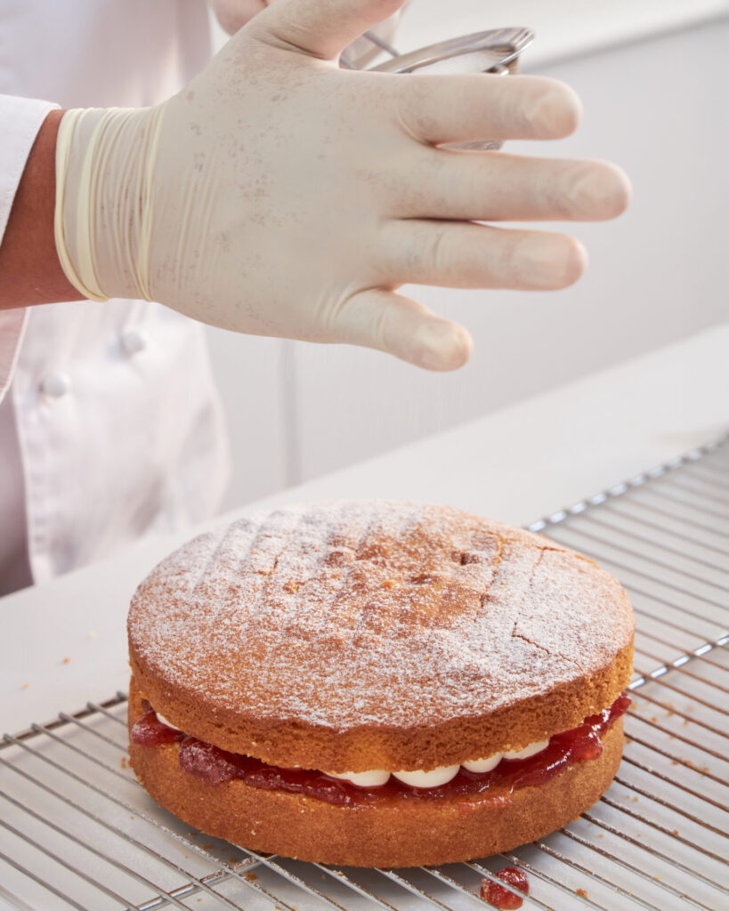 Baker dusting a Victoria sponge cake with powdered sugar at Charlotte Bakery Bangkok