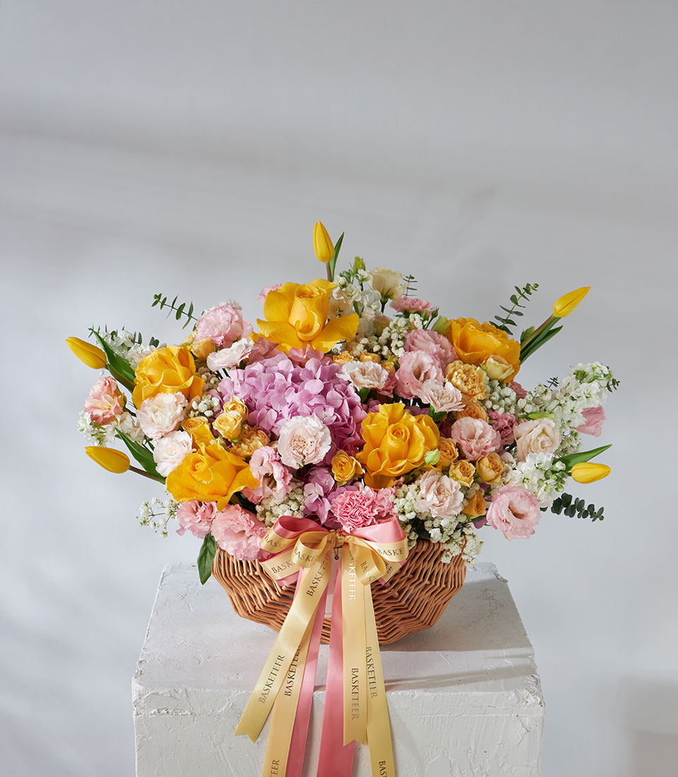 Full view of yellow and pink flower basket with Brighton Roses, pink hydrangeas, and yellow tulips tied with pastel ribbon.