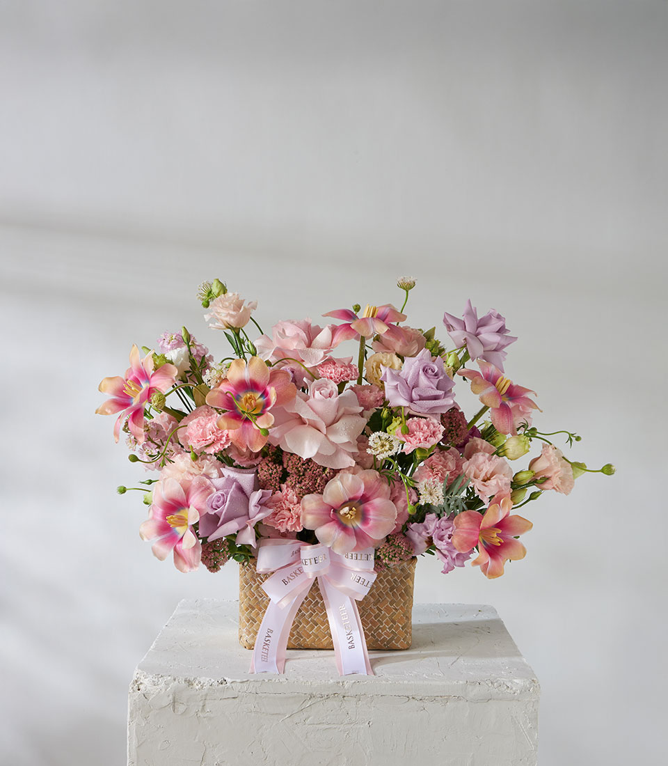 Full view of pink and lavender flower basket with imported Sweet 4 Love Roses and Ocean Song Roses arranged in a woven basket with lilac ribbon.