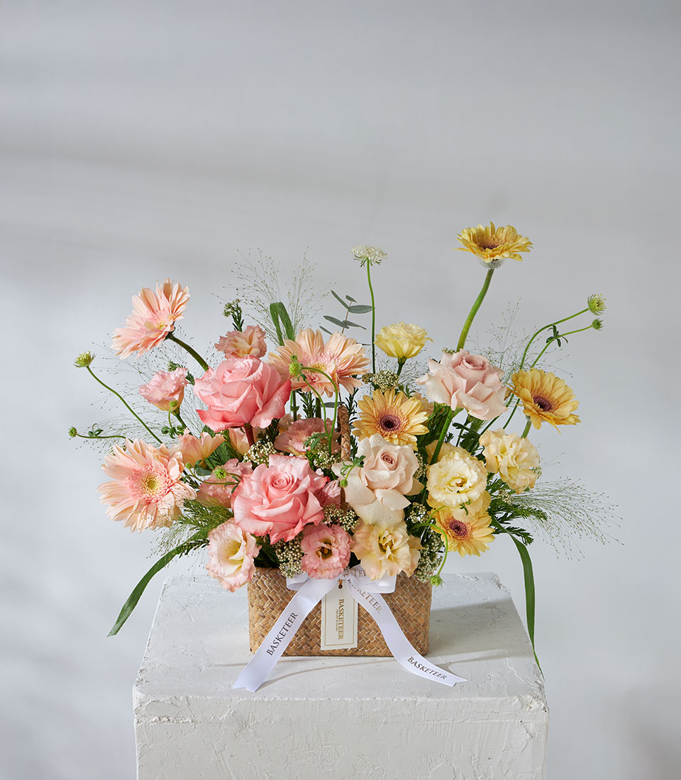 Full view of pastel peach and yellow flower basket with imported Sweet 4 Love Roses, Quicksand Roses, gerberas, and lisianthus arranged in a woven basket with white ribbon.