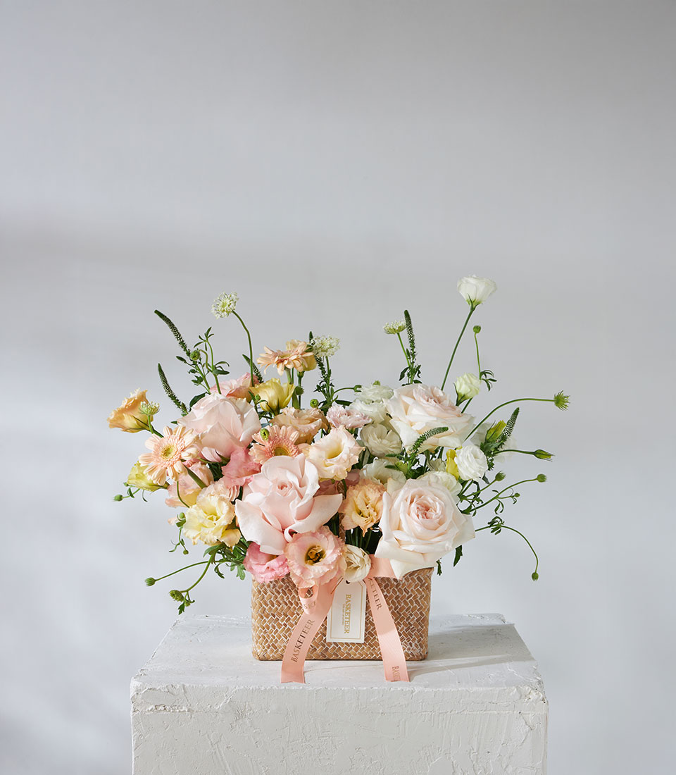 Full view of peach and ivory flower basket with imported roses, lisianthus, and ranunculus tied with a satin peach ribbon — Flowers by Basketeer.