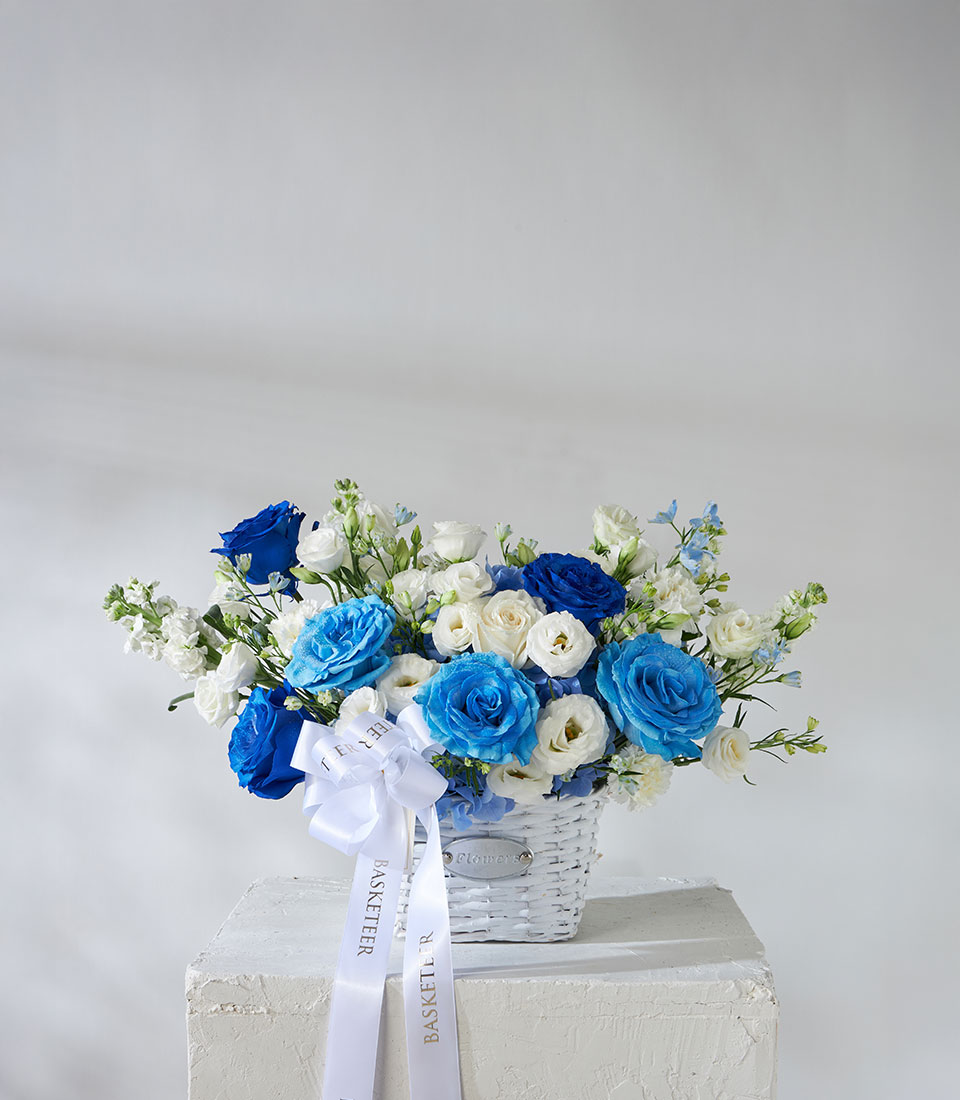 Full view of blue and white flower basket featuring imported roses from Ecuador, arranged in a white wicker basket with satin ribbon.