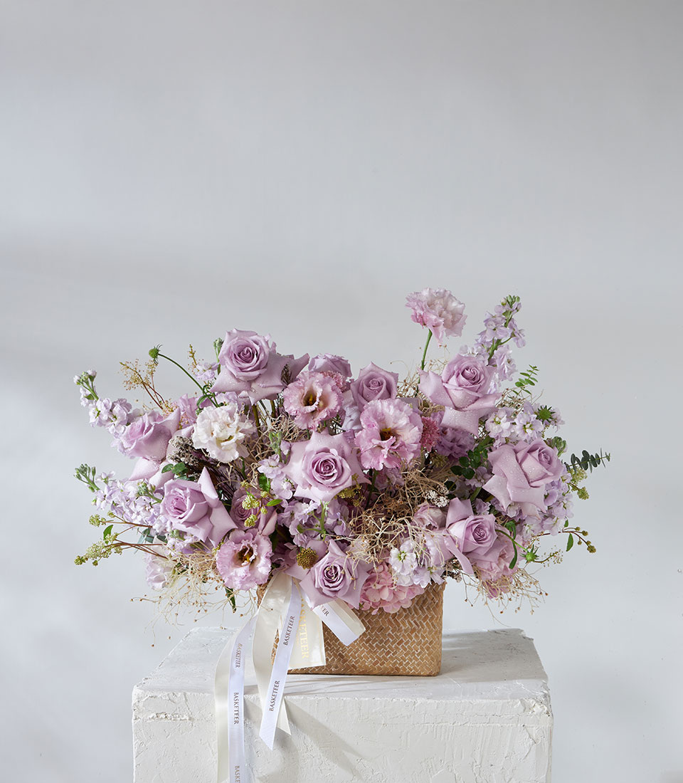 Full arrangement of lavender and pink flower basket with imported roses, hydrangeas, and lisianthus in a woven basket.