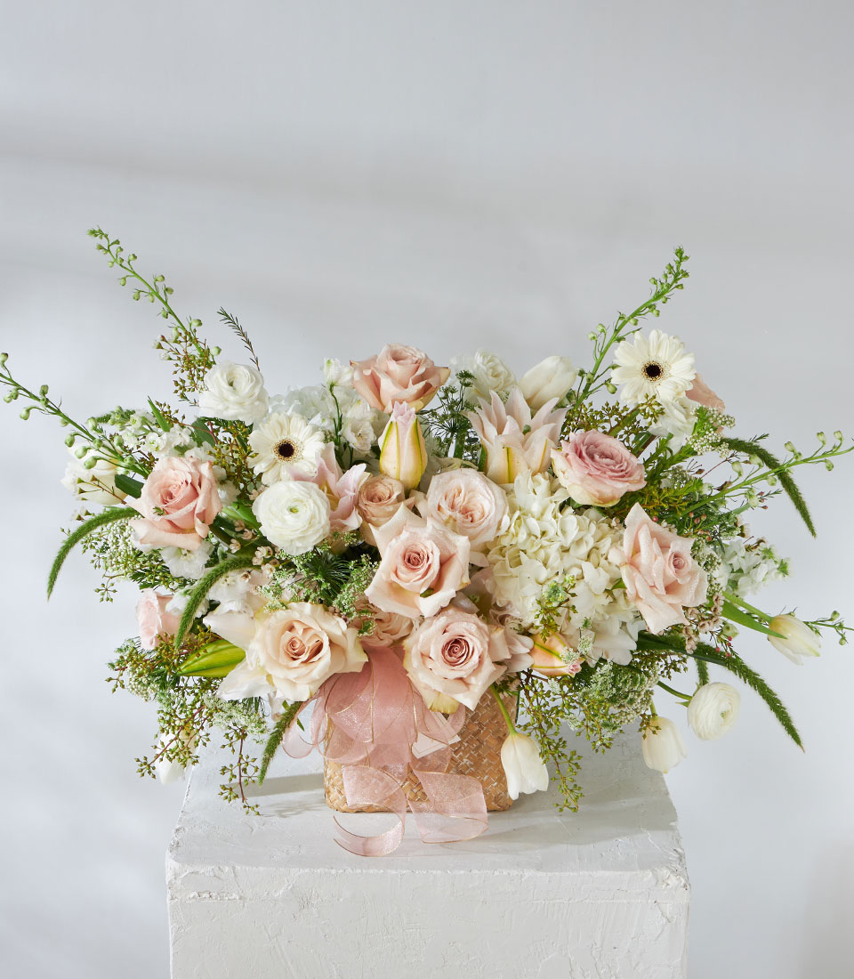 Full view of nude flower basket featuring Quicksand Roses, lilies, gerberas, and tulips arranged in woven basket with soft ribbon.