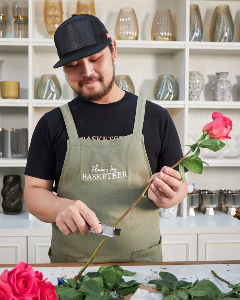 Florist from Flowers by Basketeer trimming a red rose stem