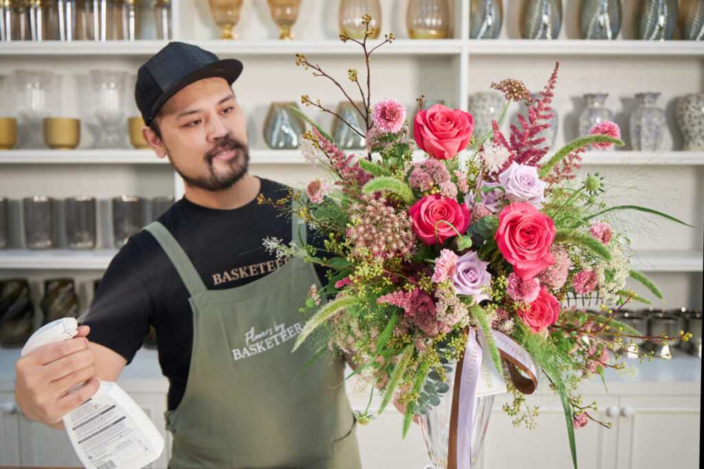 Florist from Flowers by Basketeer misting a pink and lavender flower arrangement