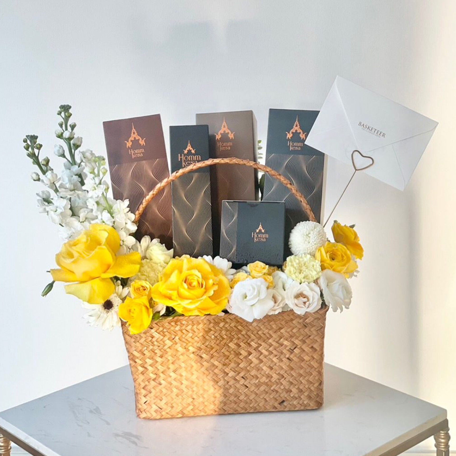 An elegant woven basket showcases premium yellow and white blooms, gourmet chocolates, and a card in a heart holder for luxury gifting in Bangkok.