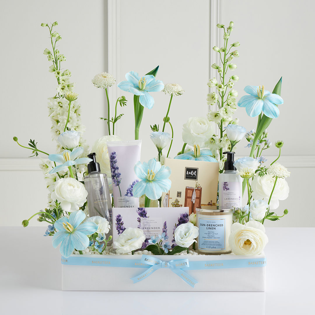 Mother’s Day gift basket with blue and white flowers, luxury spa products, and candles — beautifully arranged by Basketeer Thailand.