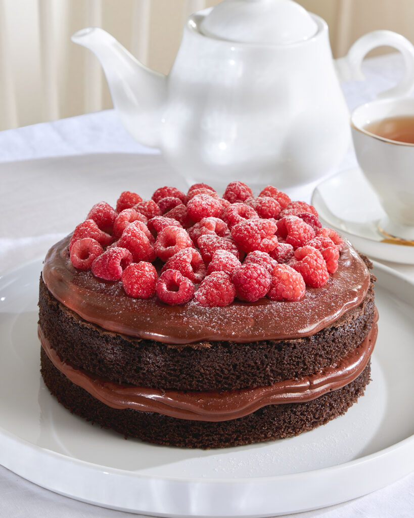 Indulge in Charlotte Bakery Bangkok’s chocolate layer cake, topped with fresh raspberries and served beside tea for true British delight.