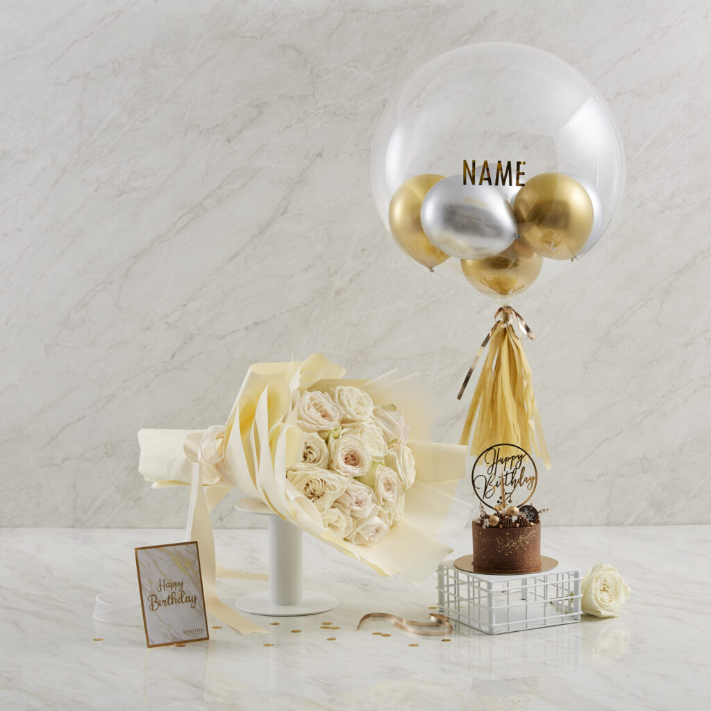 Luxurious cream rose bouquet, Charlotte Bakery chocolate birthday cake, personalised balloon, and card elegantly set on marble.