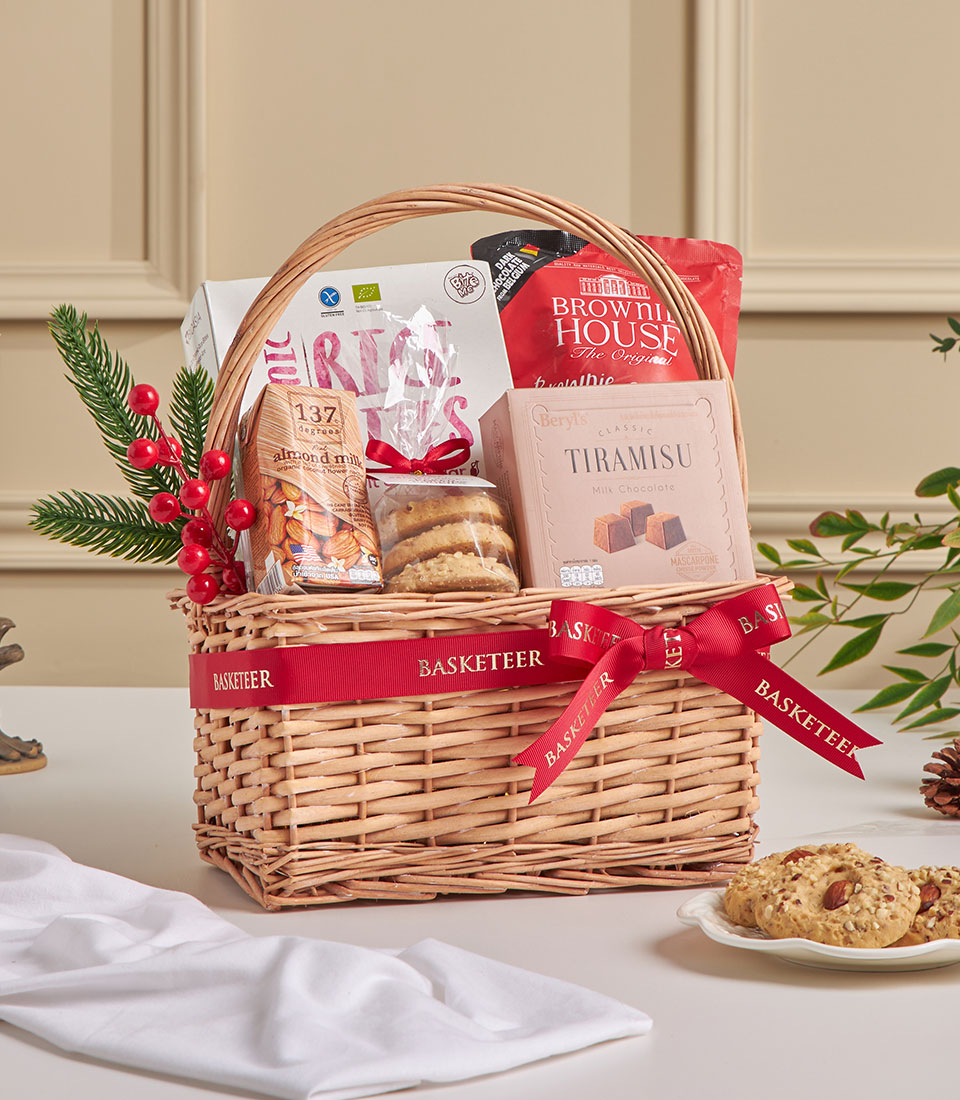 Brown wicker gift basket with cookies, tiramisu bites, rice bites, and festive decorations.