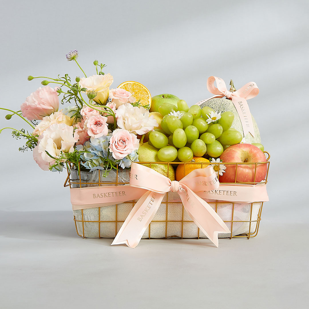Premium fruit basket by Basketeer featuring fresh seasonal fruits and pastel flower arrangements in a gold wire basket with a blush ribbon — perfect for New Year gifting and same-day delivery in Bangkok, Thailand.