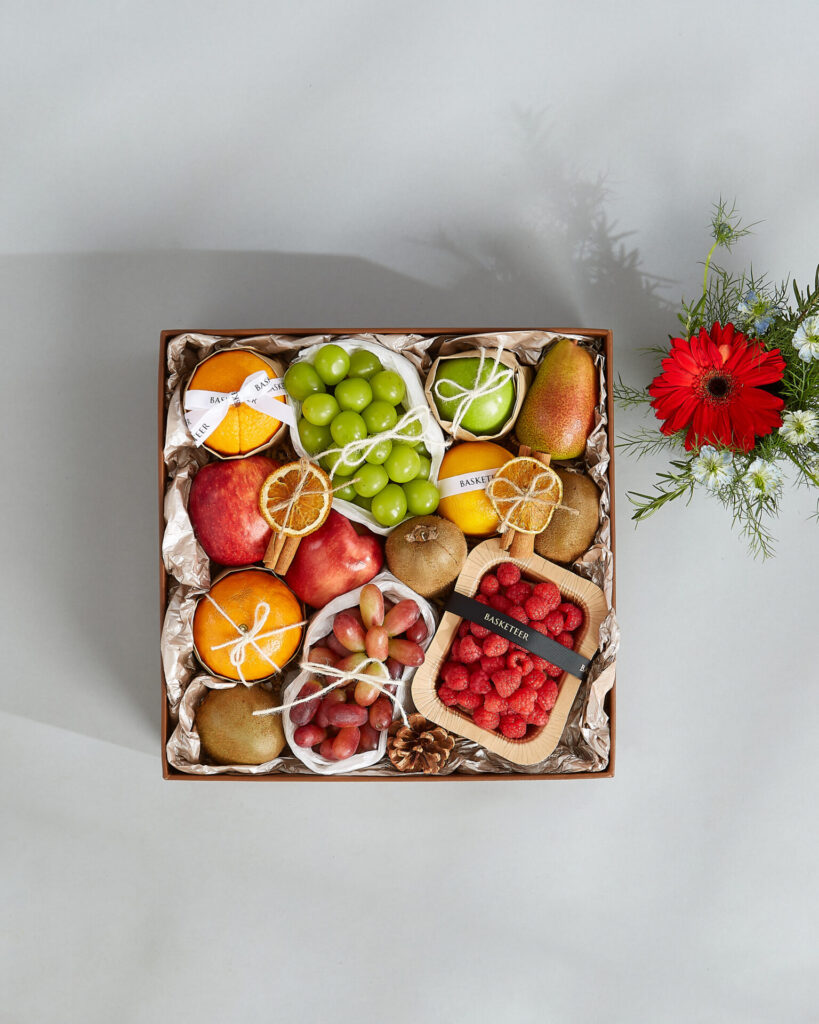 Top-view luxury fruit gift box in Bangkok by Basketeer featuring premium grapes, apples, pears, oranges, kiwis, and fresh raspberries.