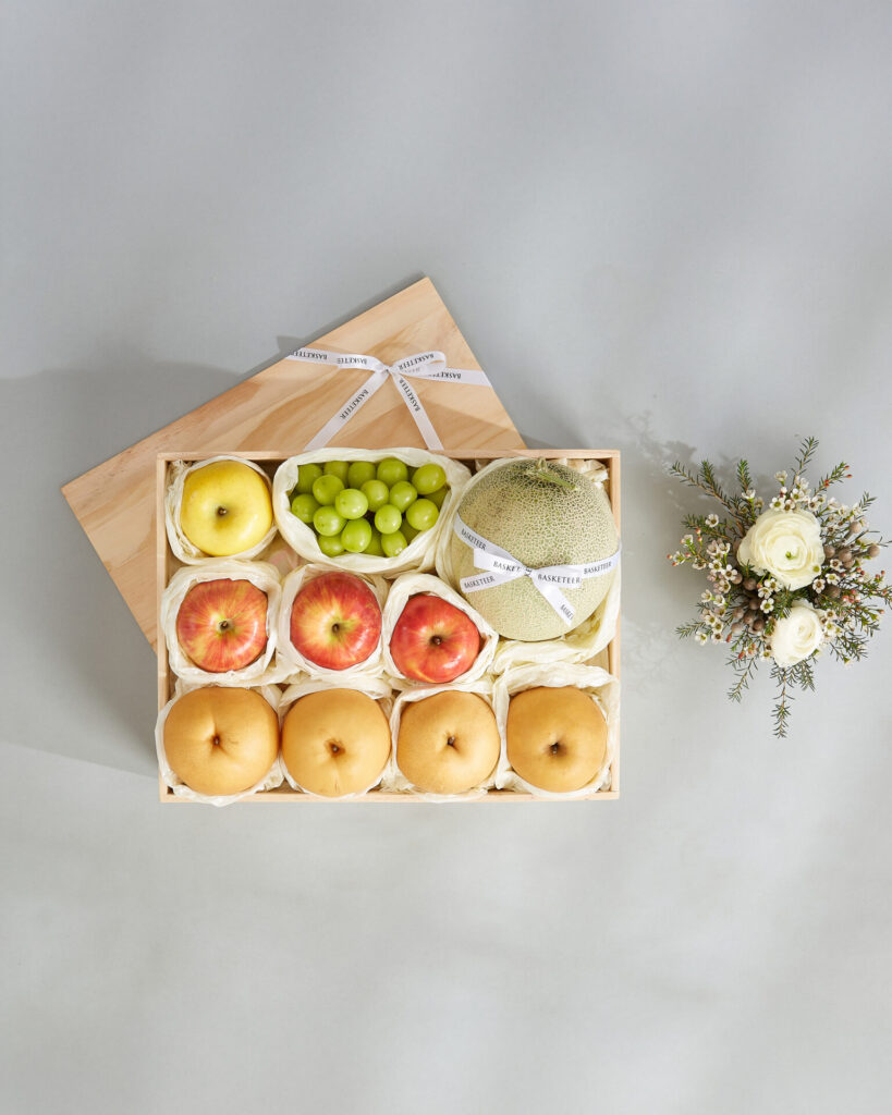 Premium Japanese fruit gift box featuring melon, Shine Muscat grapes, apples, and pears beautifully arranged in a wooden crate.