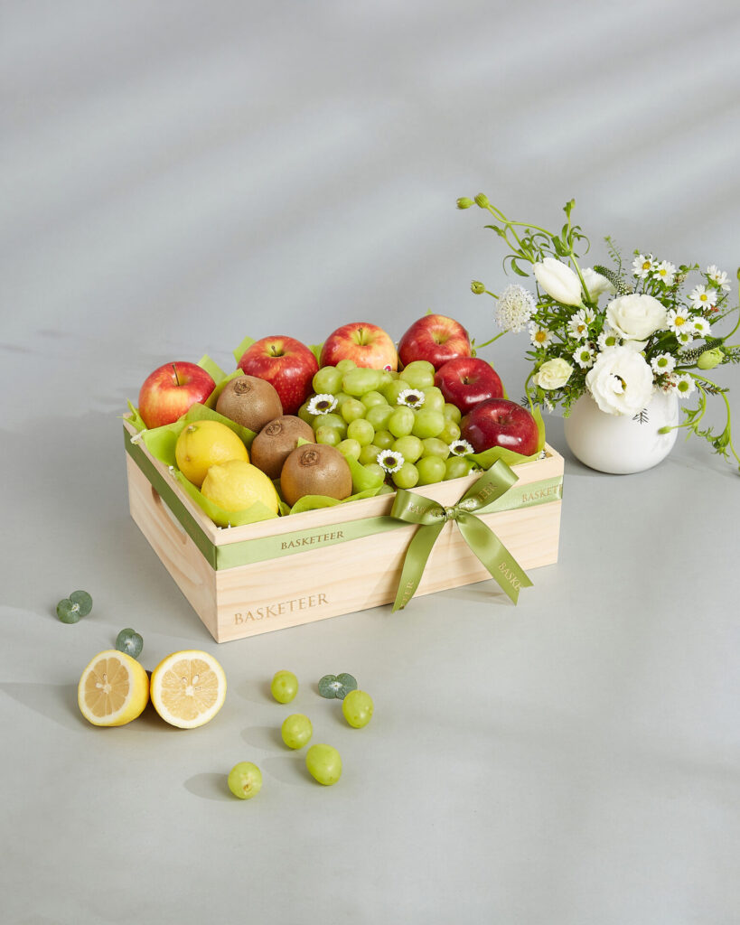 Luxury premium fruit basket featuring green grapes, apples, kiwis, and lemons arranged in a wooden crate by Basketeer.