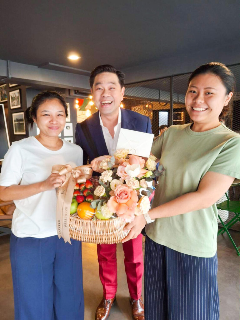 Happy customers holding a Basketeer premium fruit basket with fresh fruits and flowers.