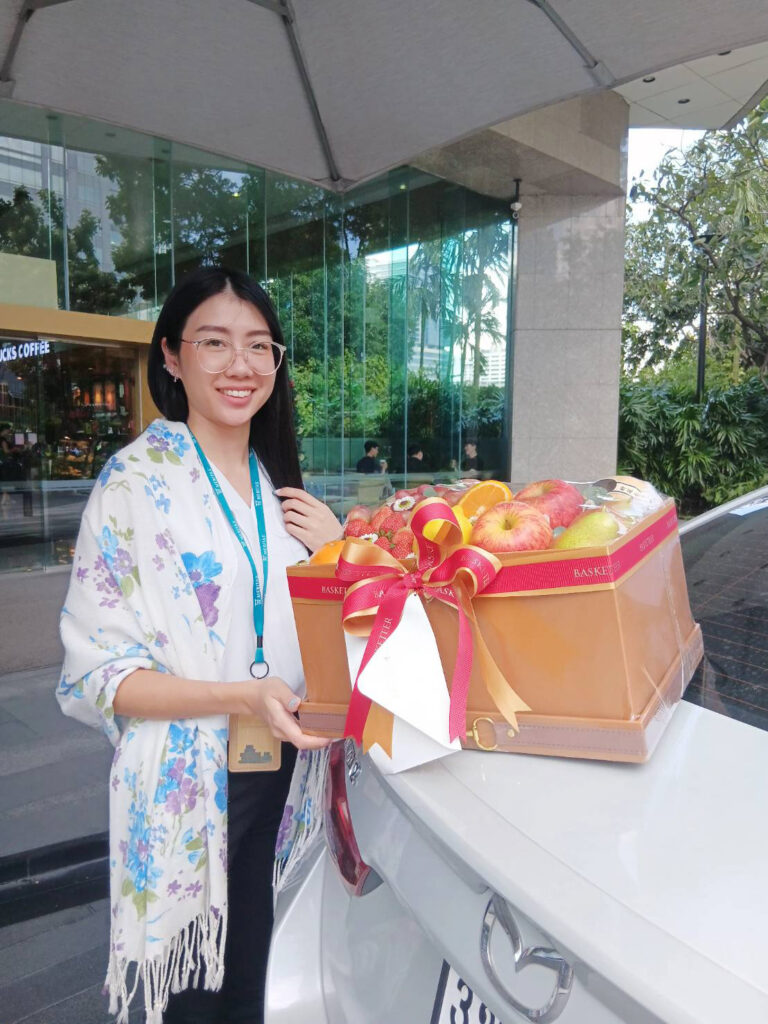 Customer holding a Basketeer premium fruit basket with apples, oranges, and fresh fruits.
