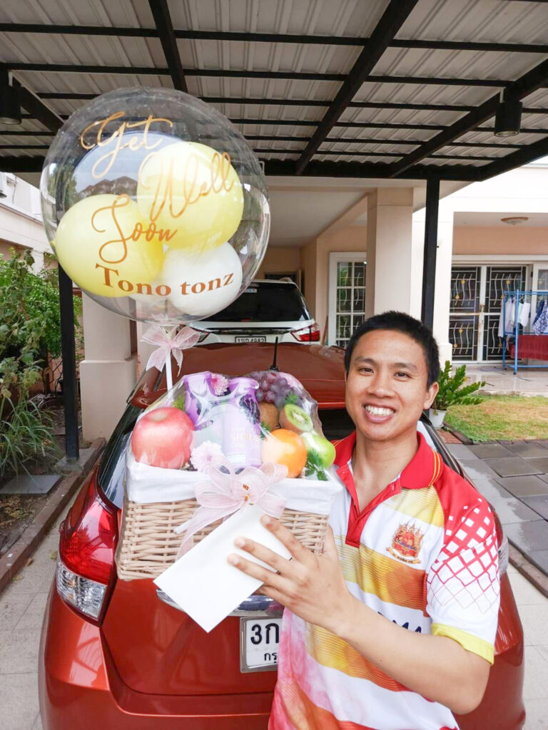 Man holding a Basketeer Get Well Soon fruit basket with a balloon.