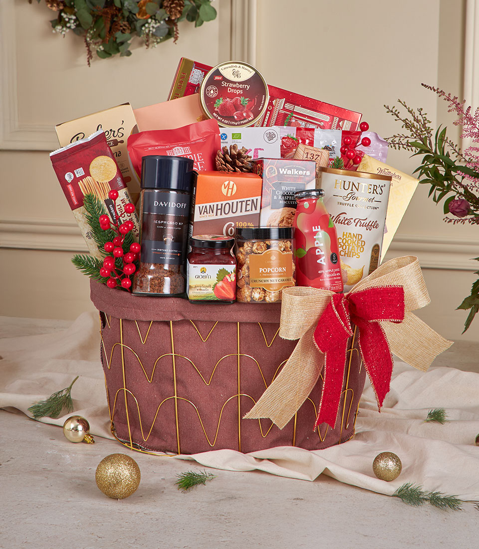 A full red Christmas hamper filled with assorted holiday treats including chocolates, cookies, nuts, snacks, and red-packaged festive items arranged in a round red basket with a gold and red bow