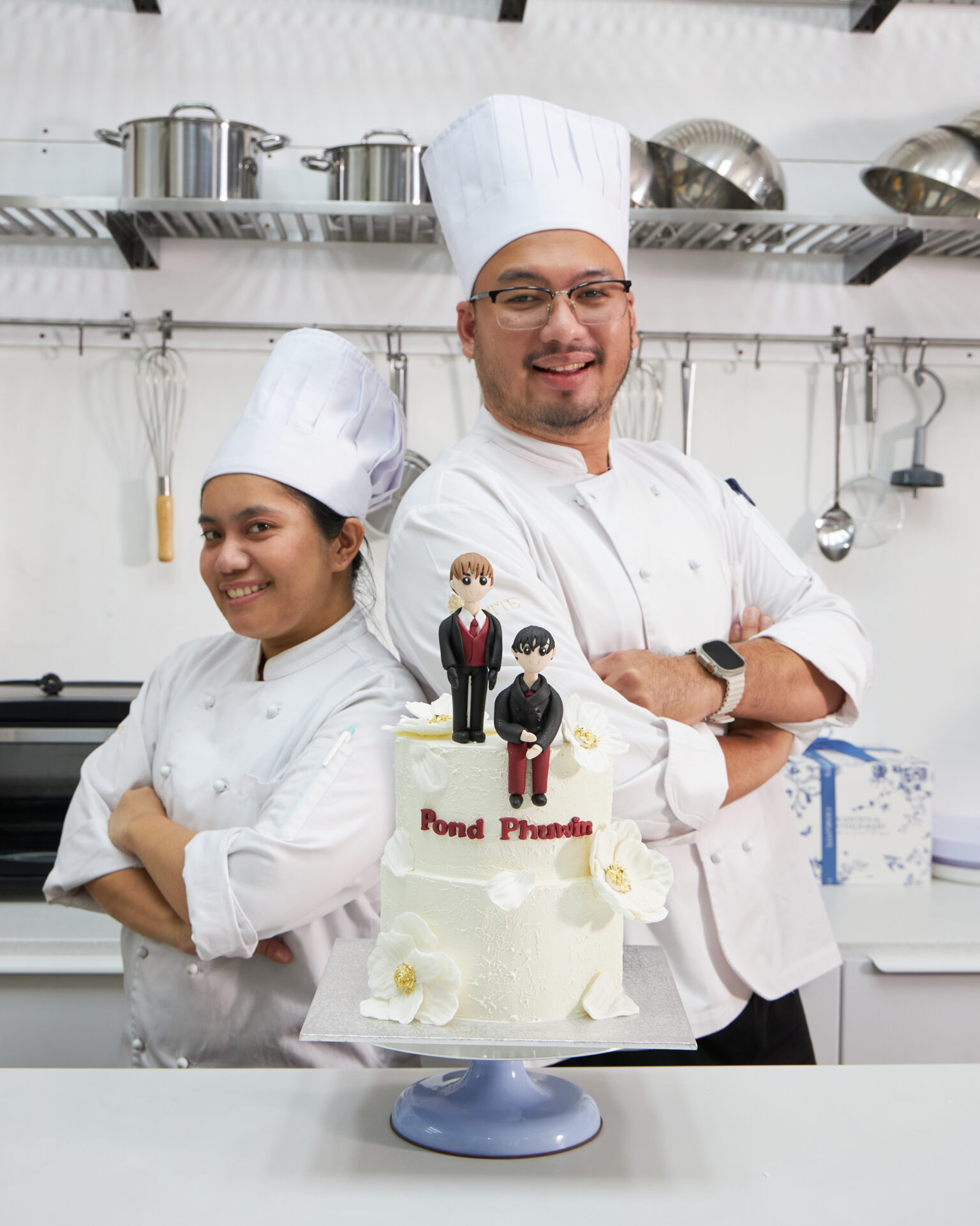 Two pastry chefs standing proudly behind a decorated celebration cake at Charlotte Bakery Bangkok