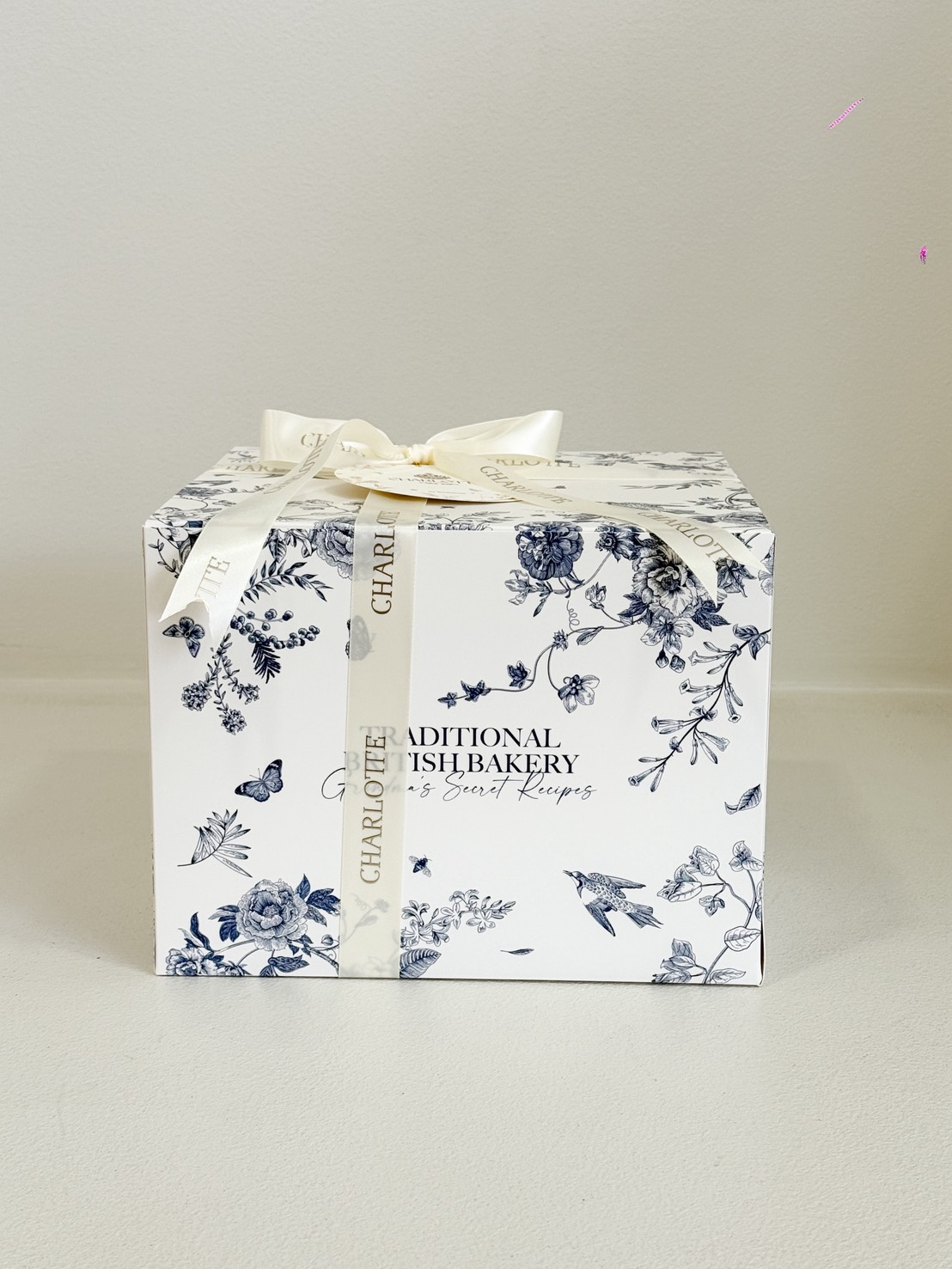 A white bakery box with blue floral patterns, tied with a white ribbon that reads 