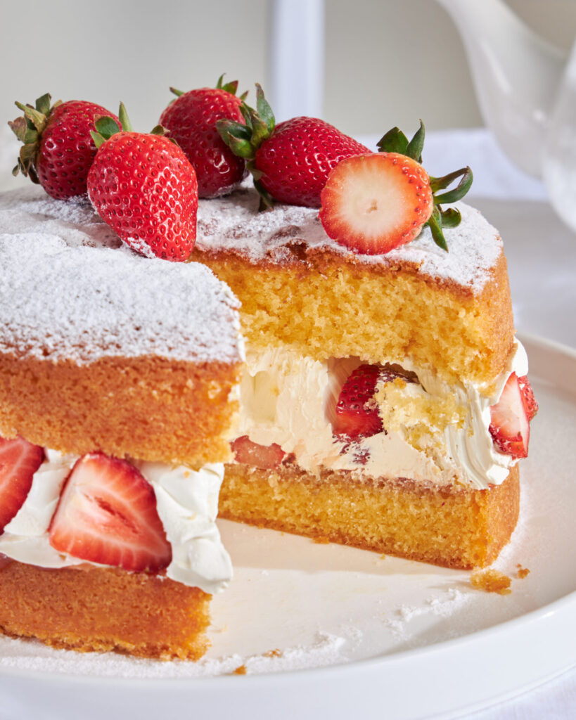 Close-up of a slice of authentic British Victoria Sponge cake showing the dense, buttery crumb texture and fresh cream filling, distinct from Thai chiffon cakes.