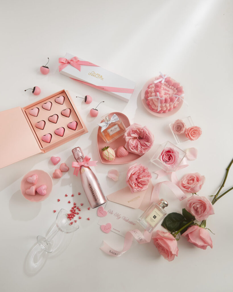 Valentine's Day flat lay featuring the Blooming Love Vanilla Heart Cake surrounded by pink roses and chocolates, a popular romantic gift combo for delivery in Bangkok.