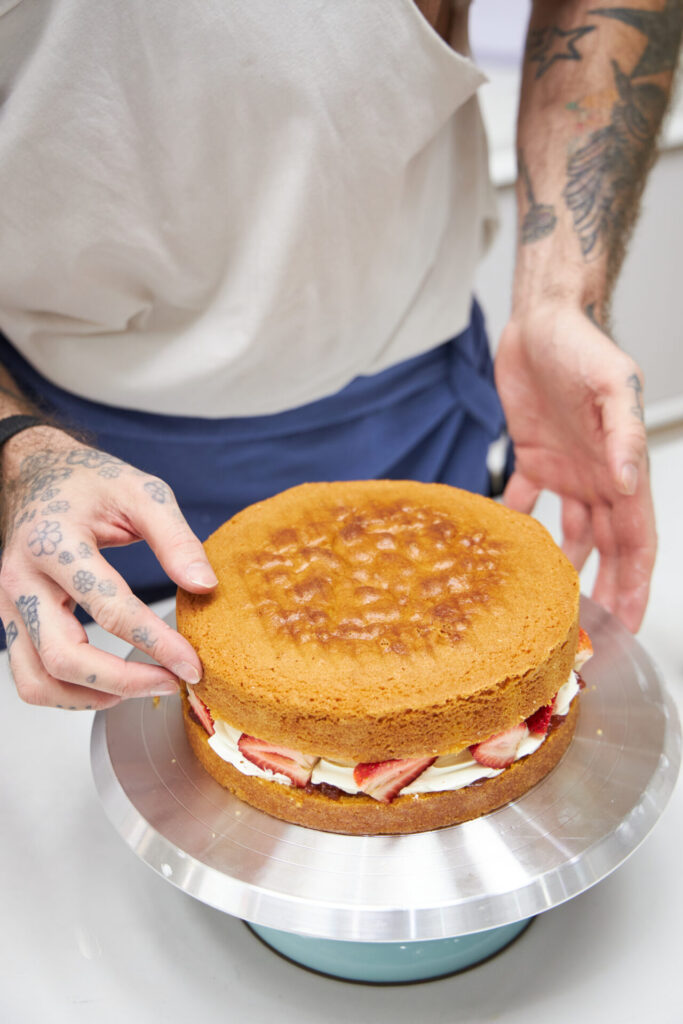 Chef Dan Stoner assembling a fresh layer cake, applying filling to a moist sponge base in the bakery kitchen