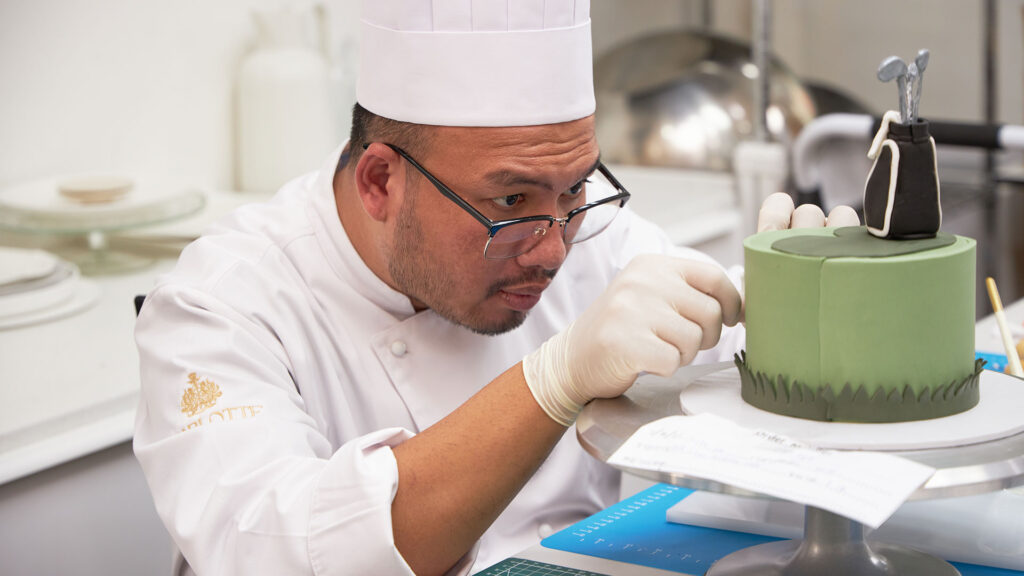 Charlotte Bakery chef hand-finishing a green golf-themed custom cake in Bangkok.