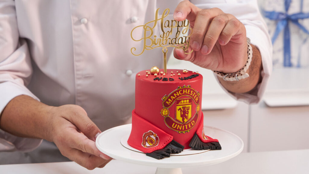 Custom Manchester United birthday cake being finished by the Charlotte Bakery chef.