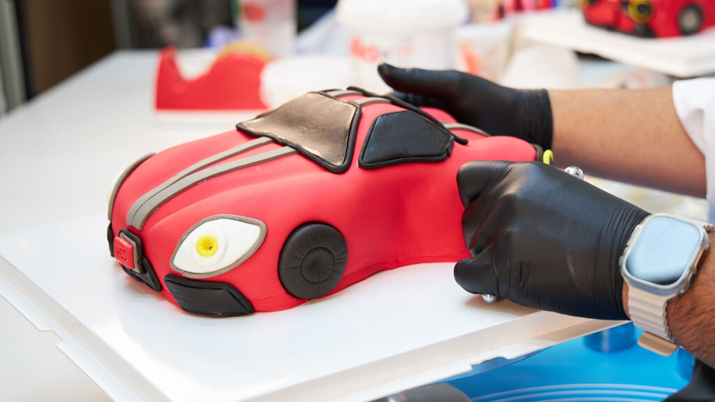 A red car-shaped custom cake being detailed by the Charlotte Bakery cake artist.