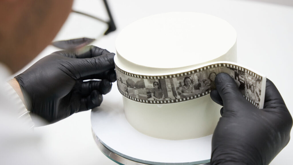 Hands applying an edible photo film strip around a Charlotte Bakery custom cake.