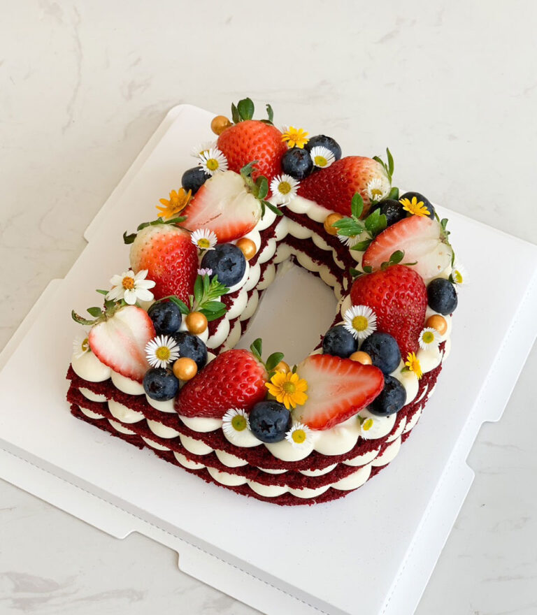 Letter D red velvet cake with strawberries, blueberries, and flowers by Charlotte Bakery