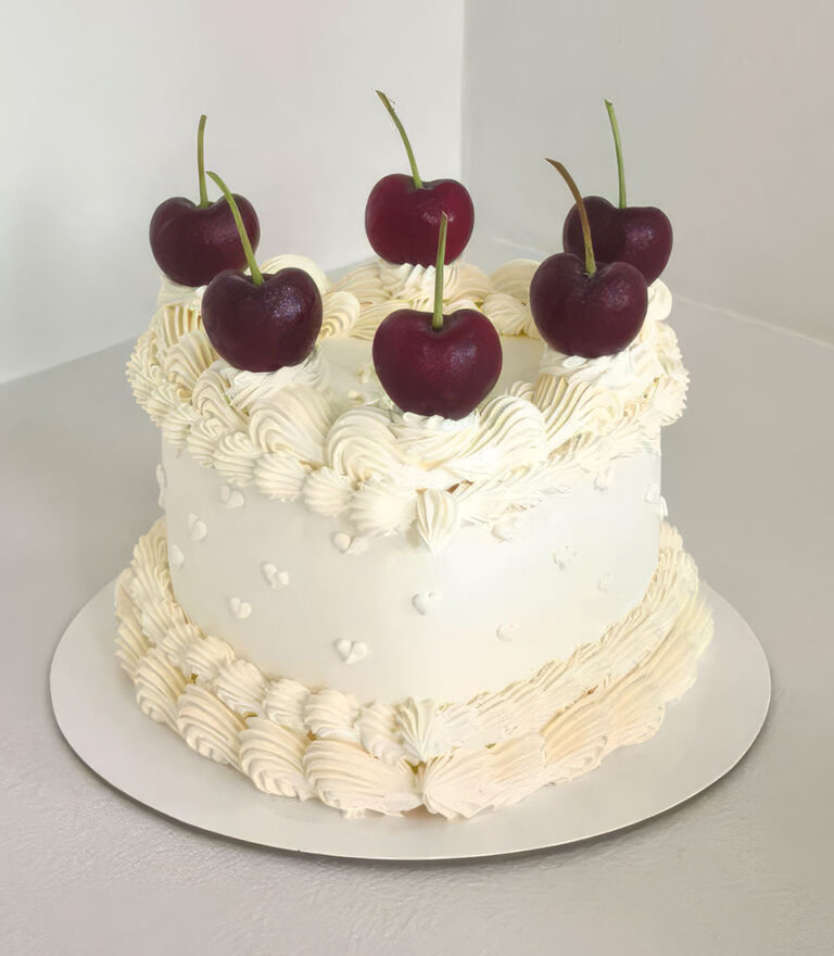 Vintage-style white cake topped with cherries and buttercream piping by Charlotte Bakery