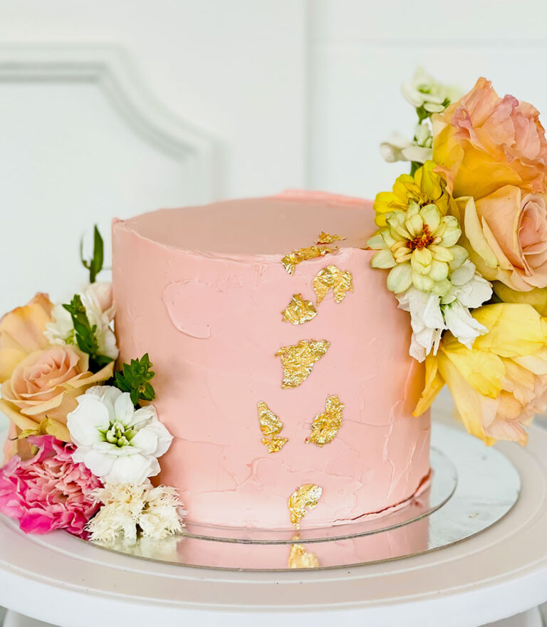 Peach buttercream cake with fresh flowers and gold leaf accents by Charlotte Bakery